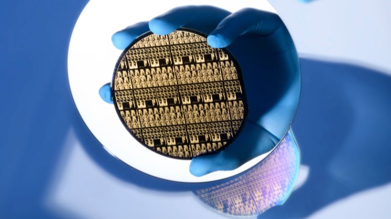 Gloved hand holding an indium phosphide photonic wafer with blue laboratory lighting
